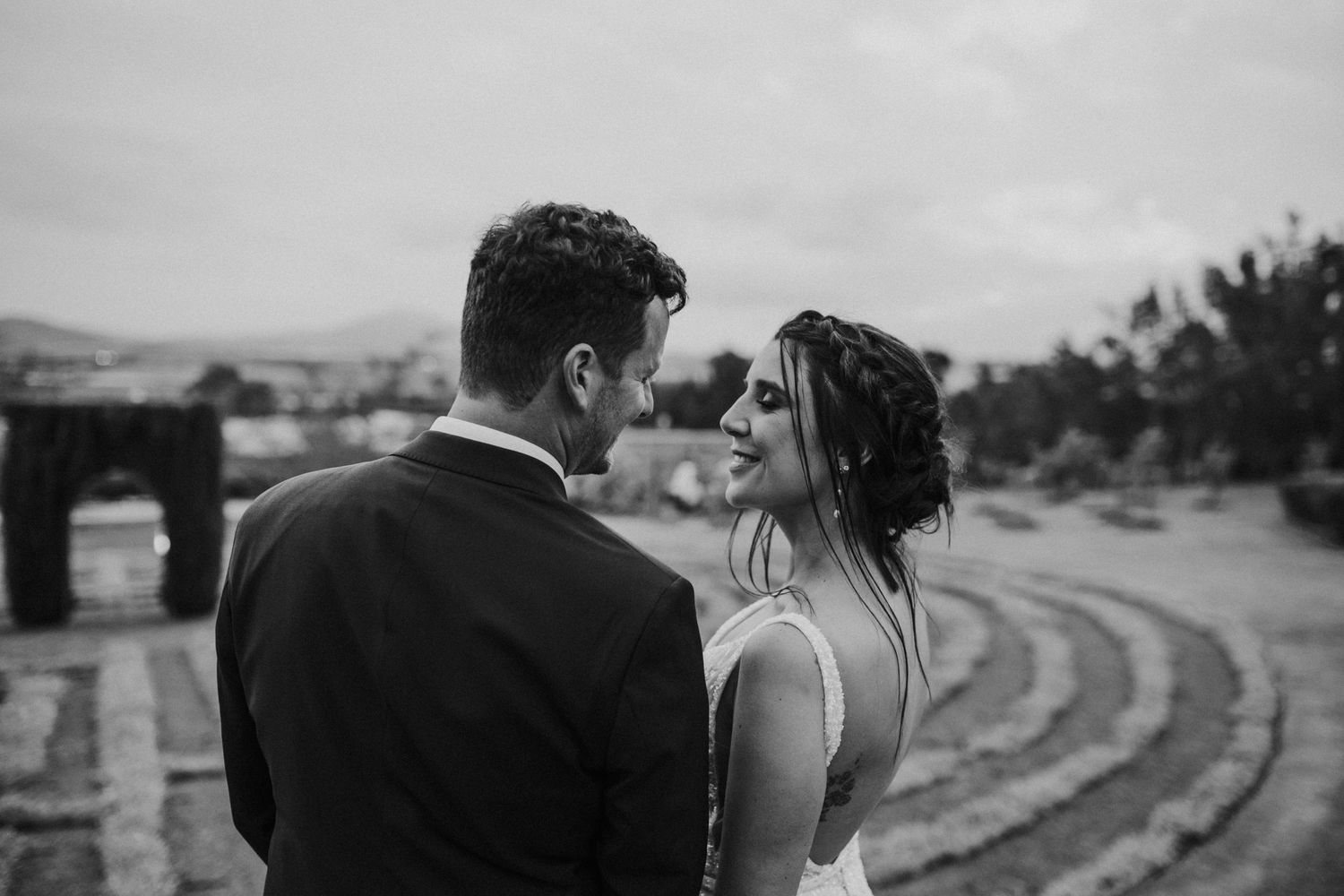Black and white romantic wedding portrait of couple gazing at each other with scenic backdrop.