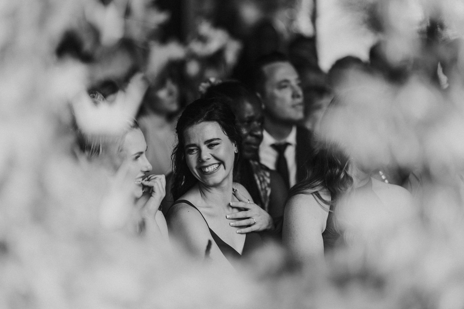 Black and white photo of wedding guests laughing emotionally during outdoor ceremony.