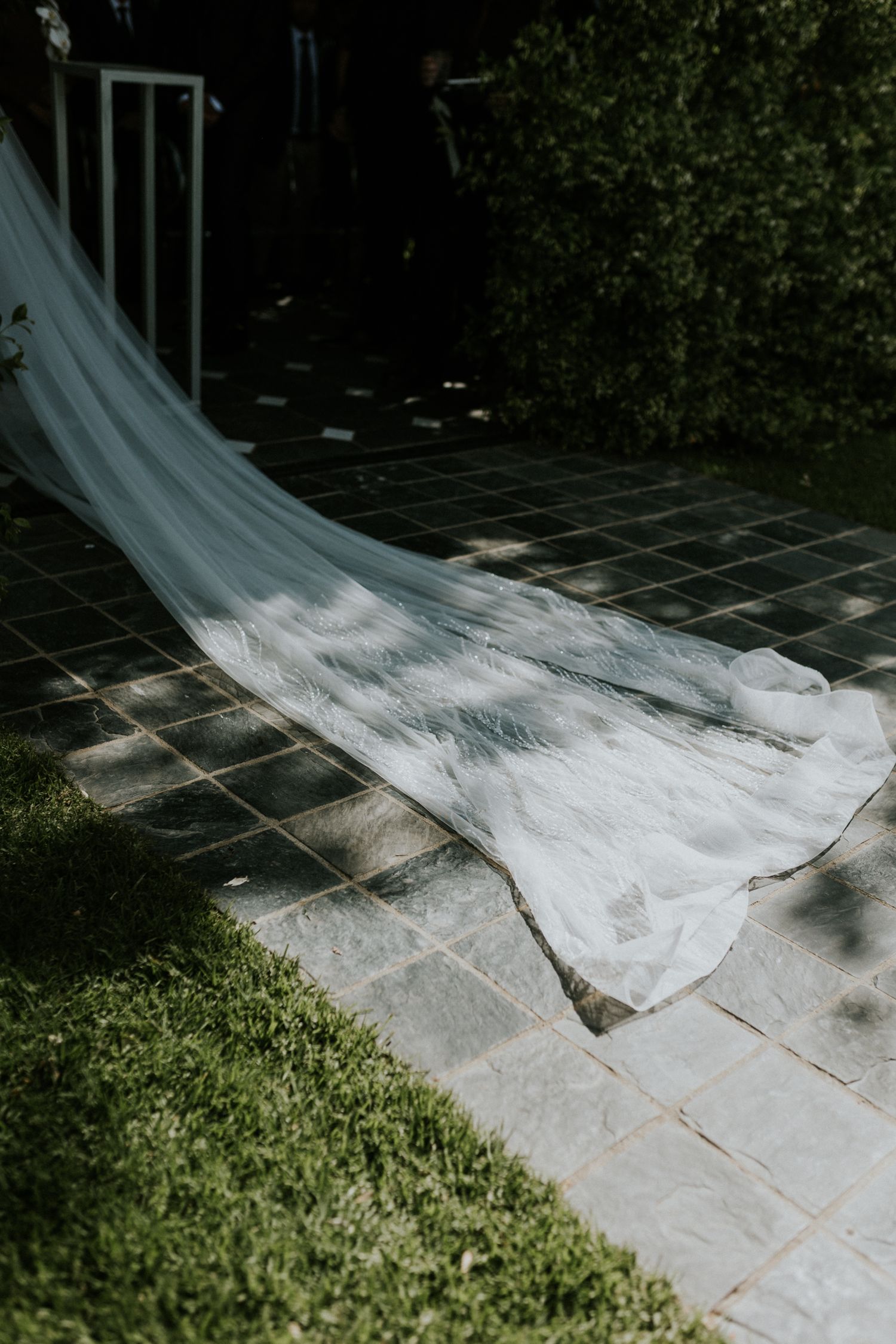 Long white bridal veil trails elegantly across a tiled outdoor patio at a wedding venue.