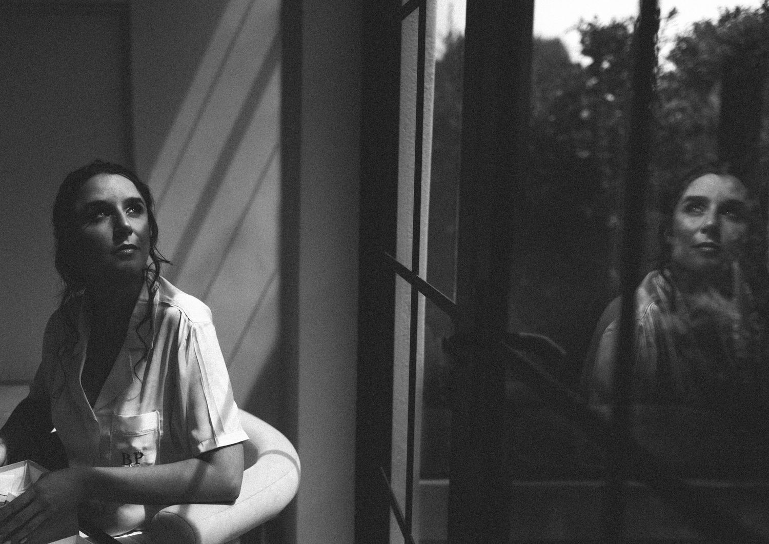 Black and white portrait of bride reflected in window light before wedding.
