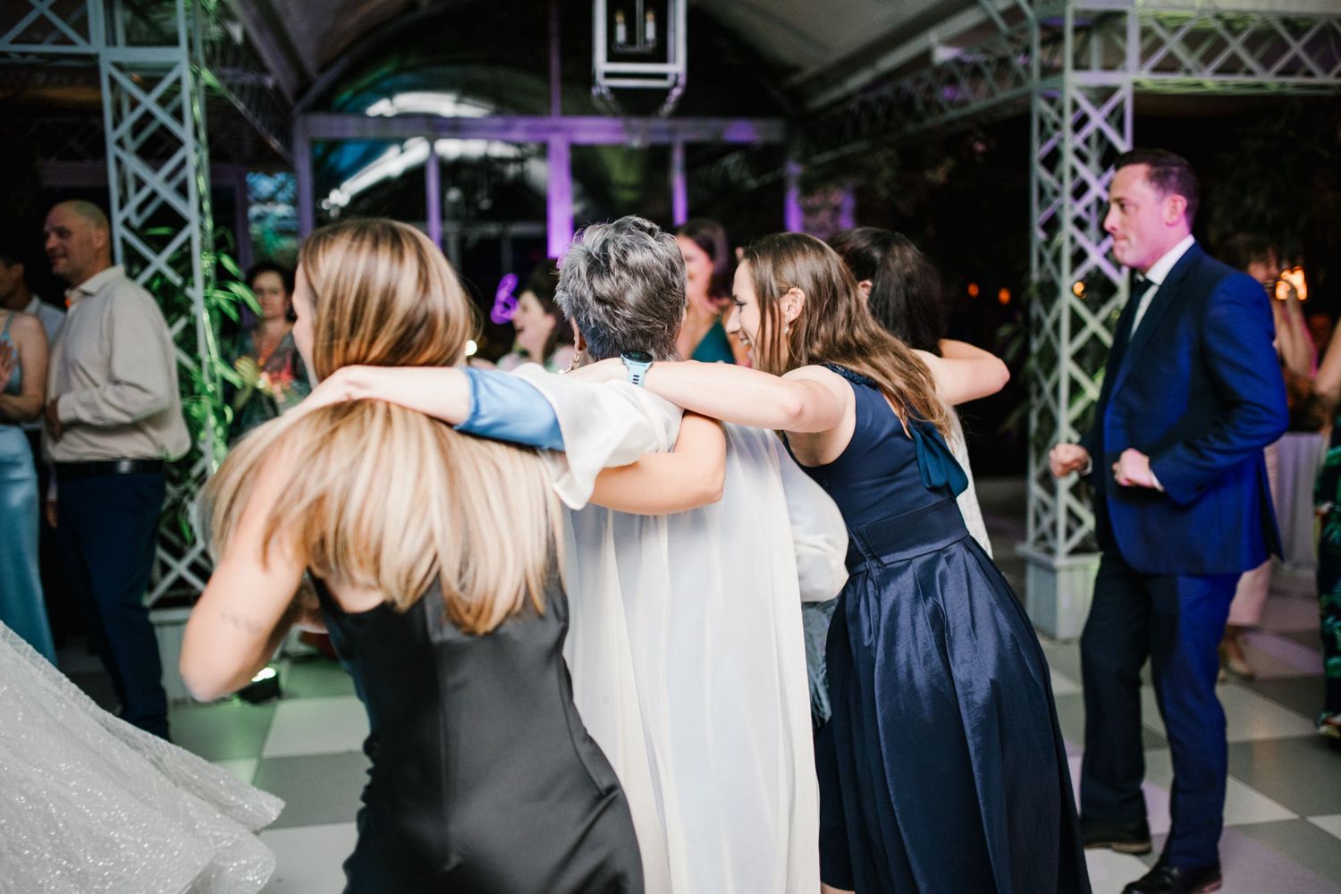 Group of women hugging on dance floor at colorful wedding reception party.