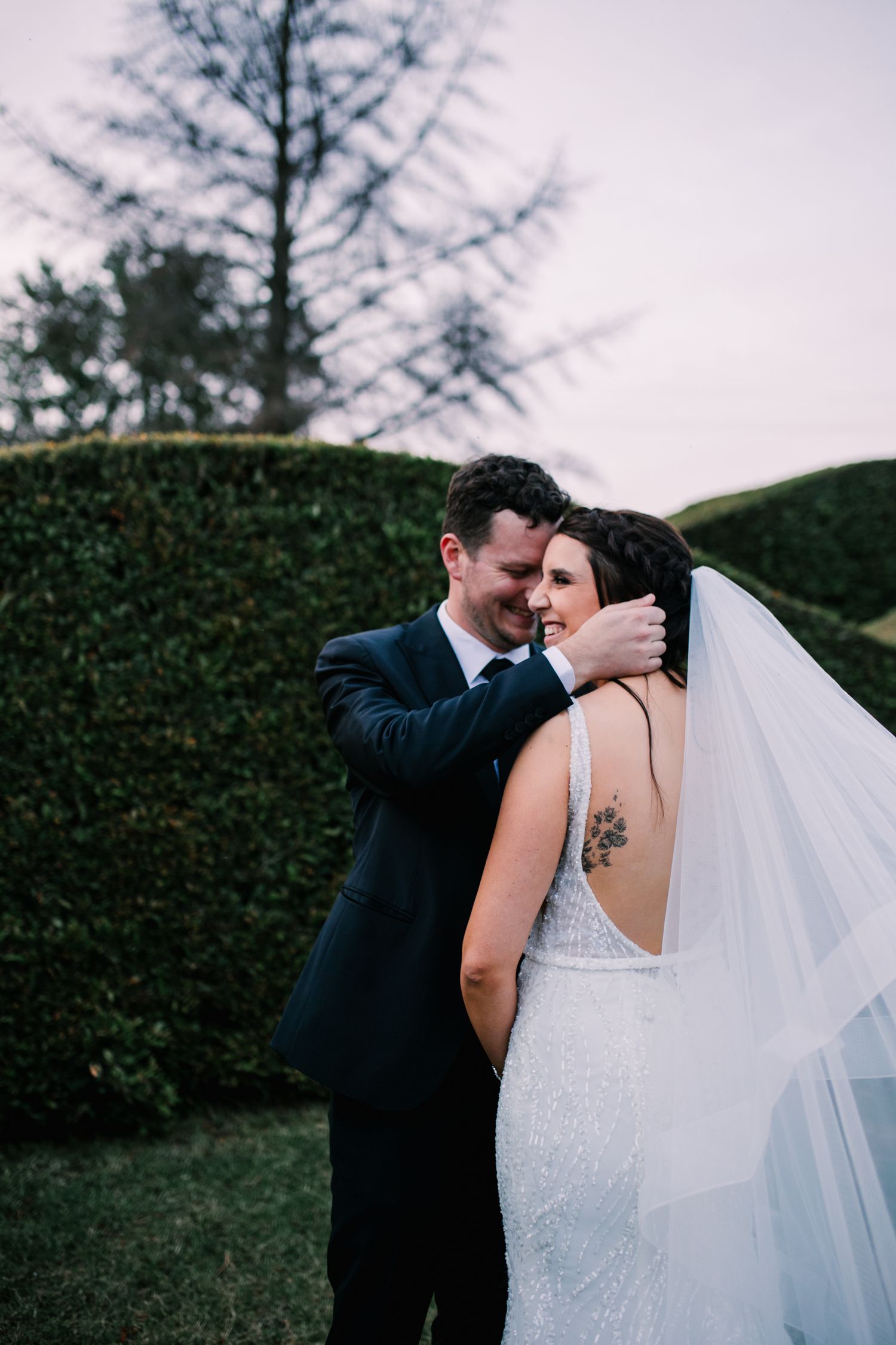 Groom tenderly embracing bride with tattoo visible on her back in a romantic wedding portrait.
