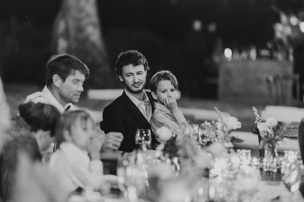 Wedding guests gathered around candlelit table during elegant outdoor evening reception dinner.