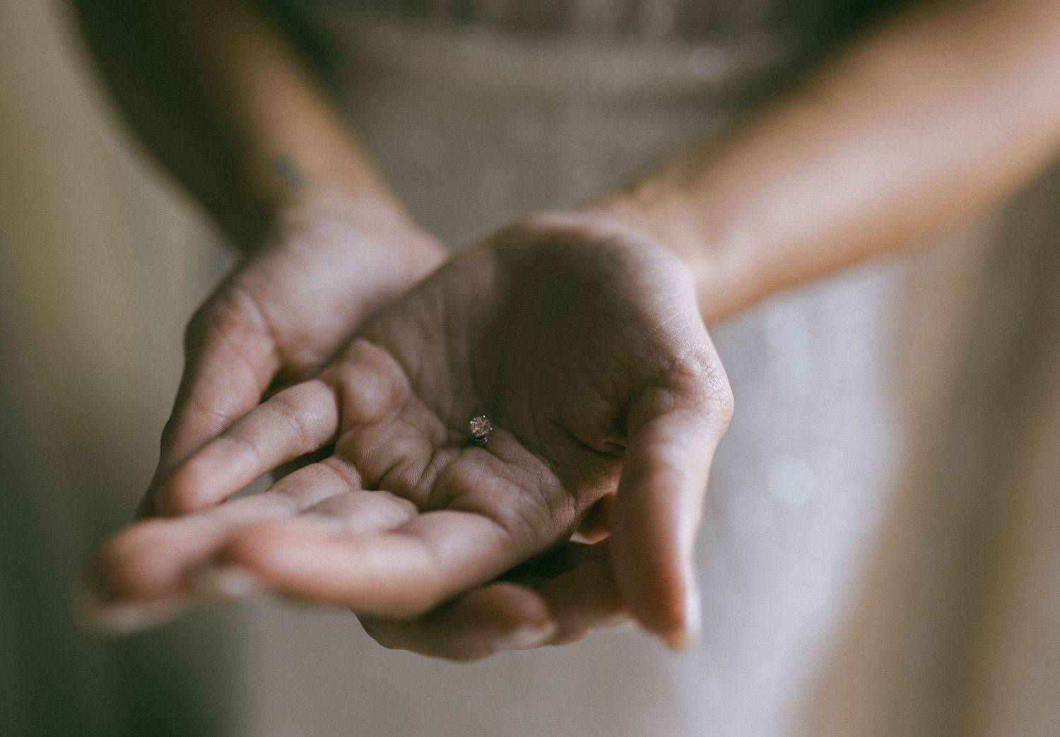 Close-up of hands gently holding a small diamond engagement ring as a precious gift.