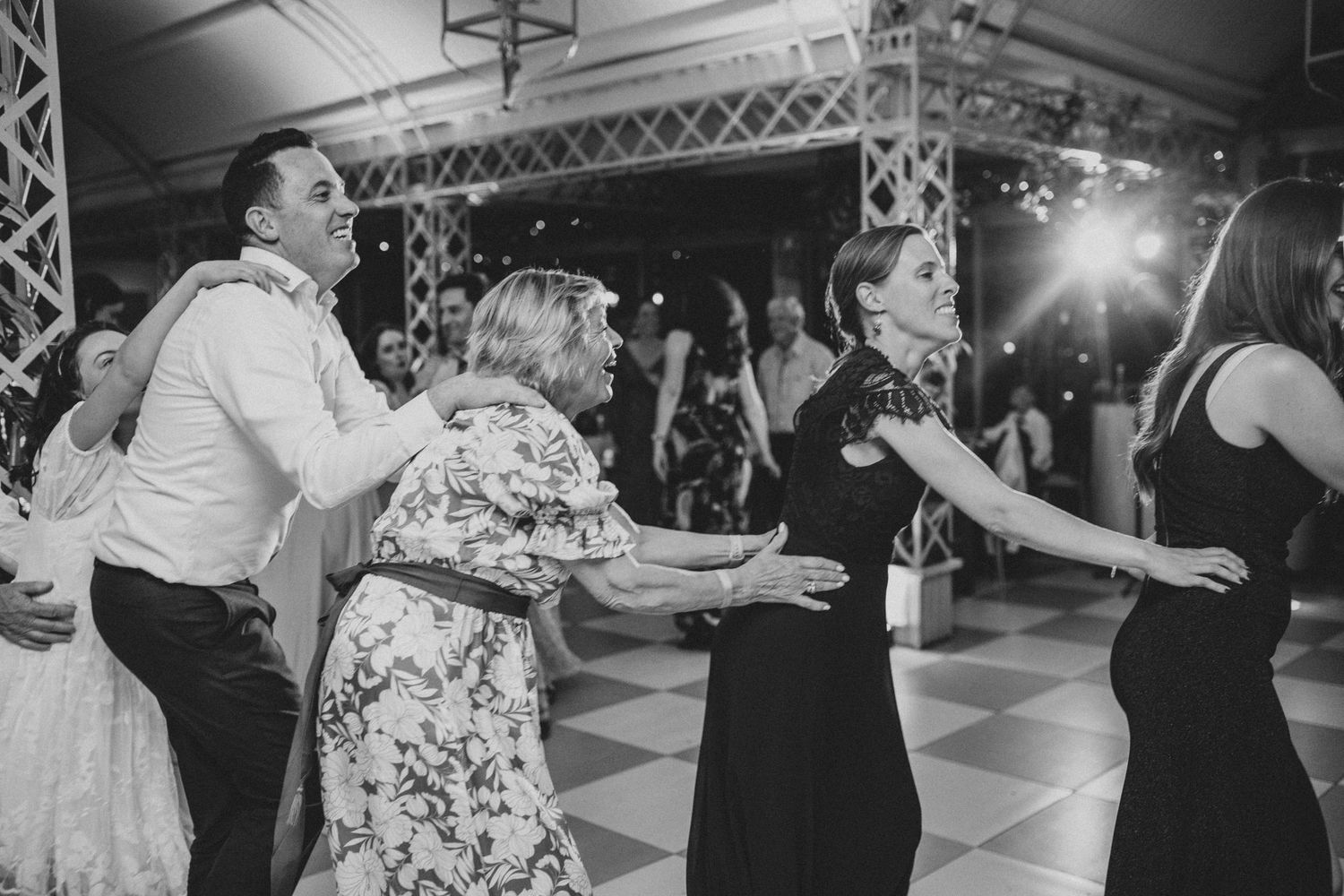 Wedding guests dance energetically together on checkered dance floor at lively reception party.