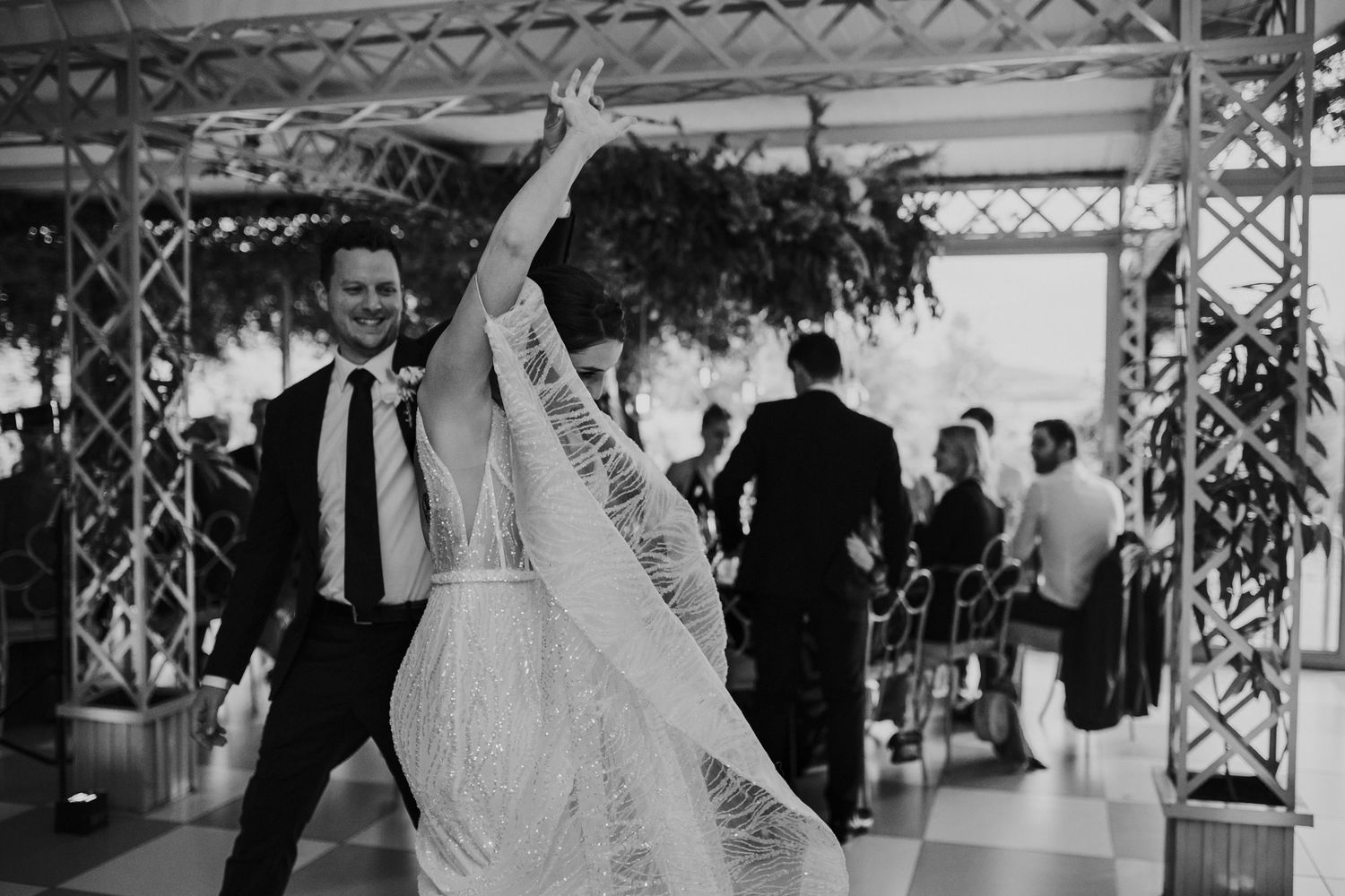 Bride twirling her lace veil with groom laughing during wedding reception entrance in black and white.