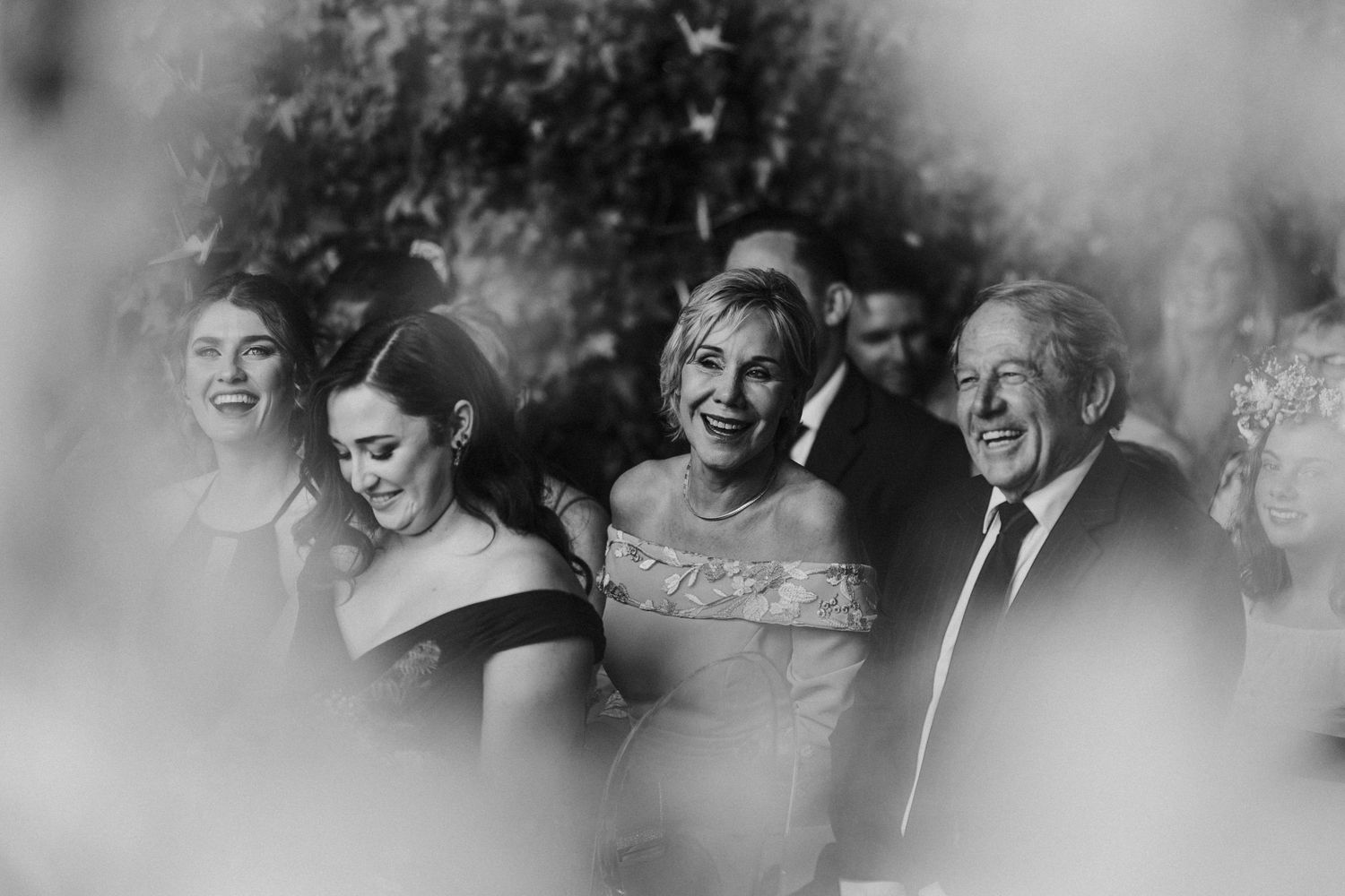 Black and white photo of joyful wedding guests laughing together during outdoor ceremony celebration.