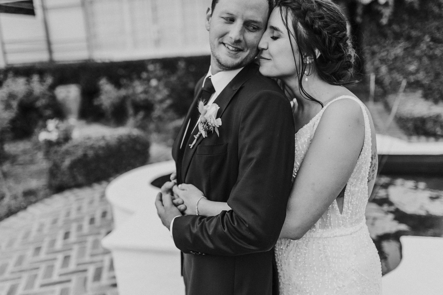 Black and white wedding portrait of smiling couple embracing tenderly in a beautiful garden setting.