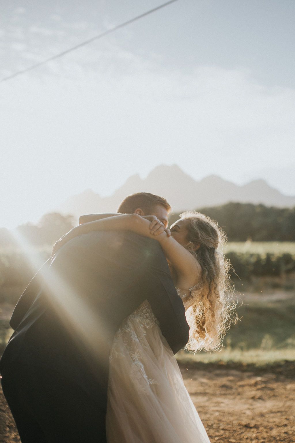 Bride and groom sharing a kiss in golden sunlight with mountain vineyard in the background.