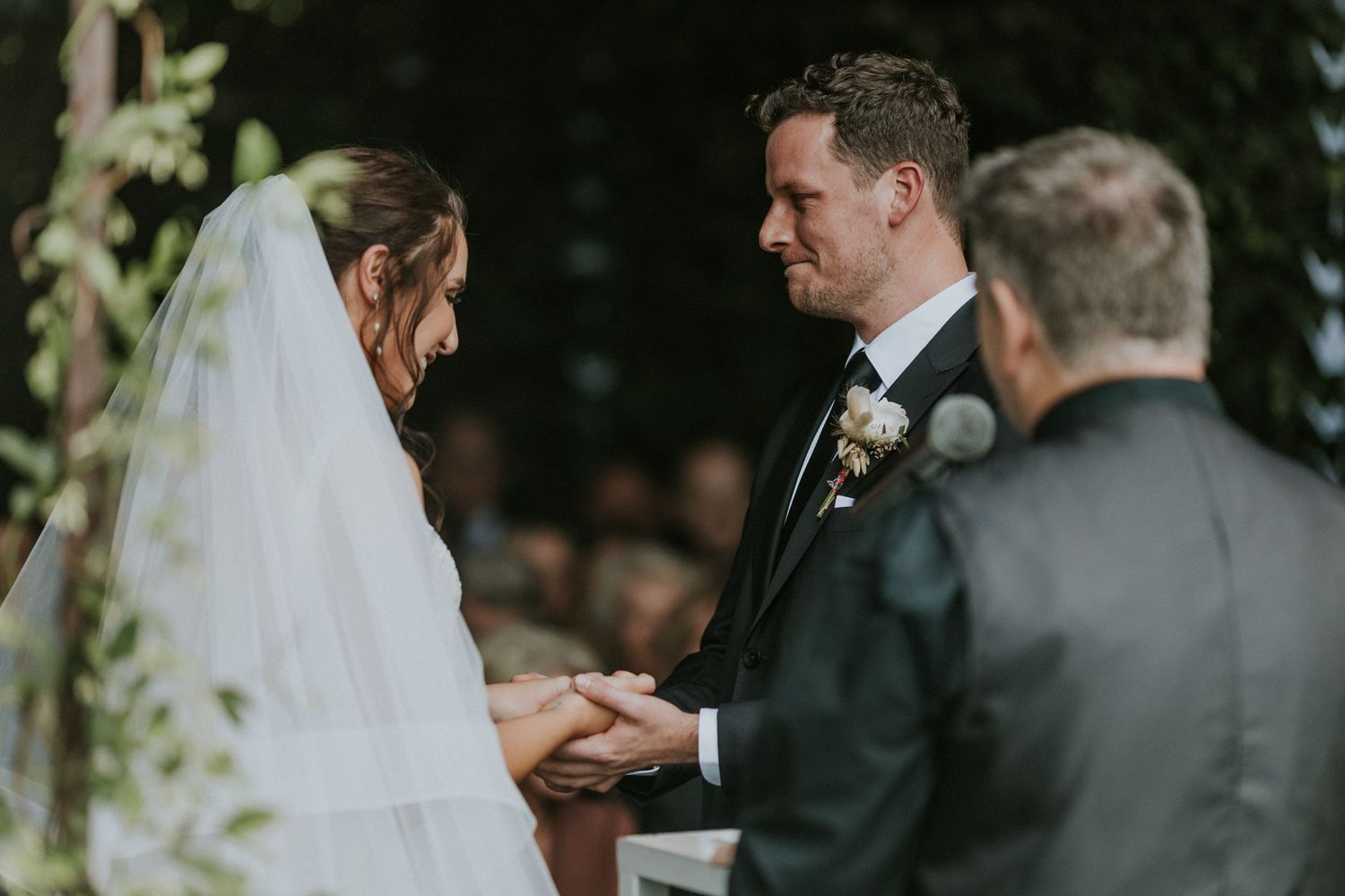 Bride and groom hold hands tenderly during their outdoor wedding ceremony exchanging vows.