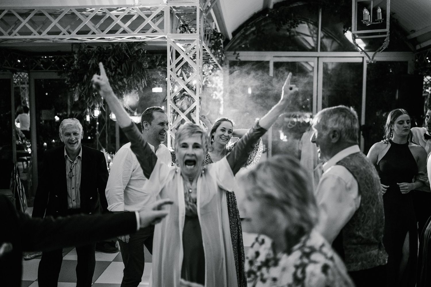 Joyful wedding guest celebrating with arms raised surrounded by cheering crowd.