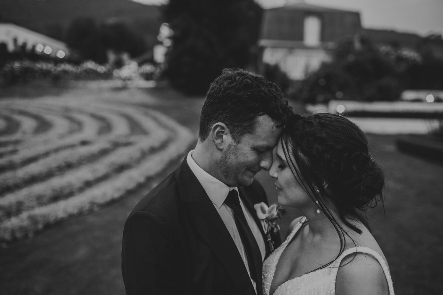 Intimate black and white close-up of bride and groom touching foreheads tenderly at dusk.