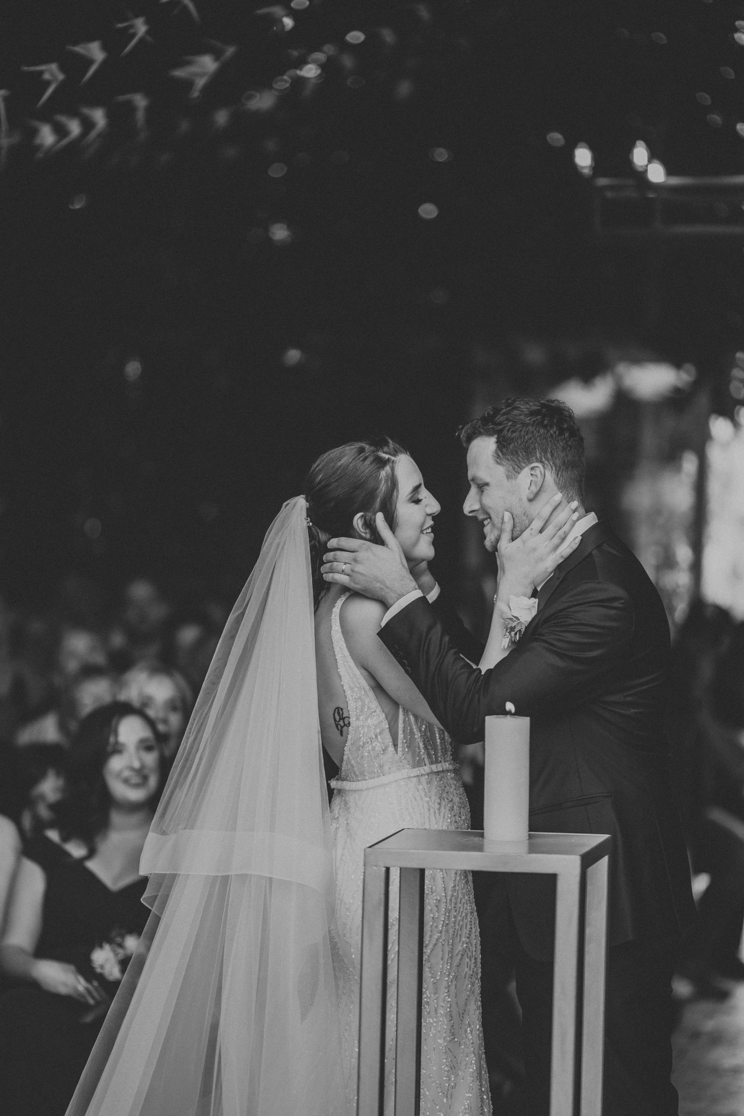 Bride and groom share tender moment holding each others faces at wedding altar.