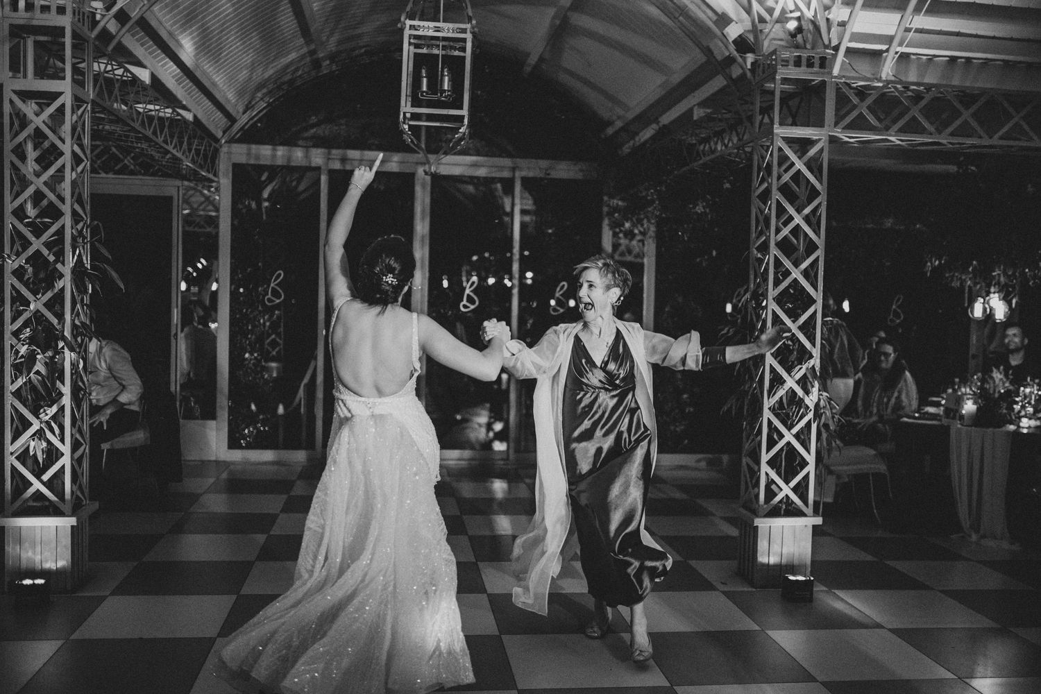 Bride and guest dancing together on checkered dance floor at elegant wedding reception in black and white photo.
