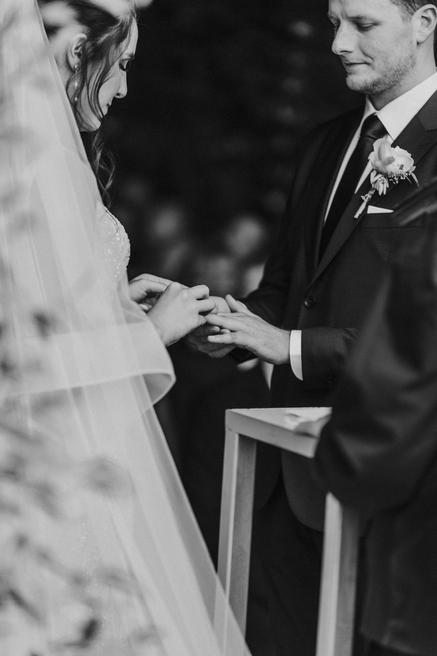 Groom places wedding ring on brides finger during elegant outdoor wedding ceremony.