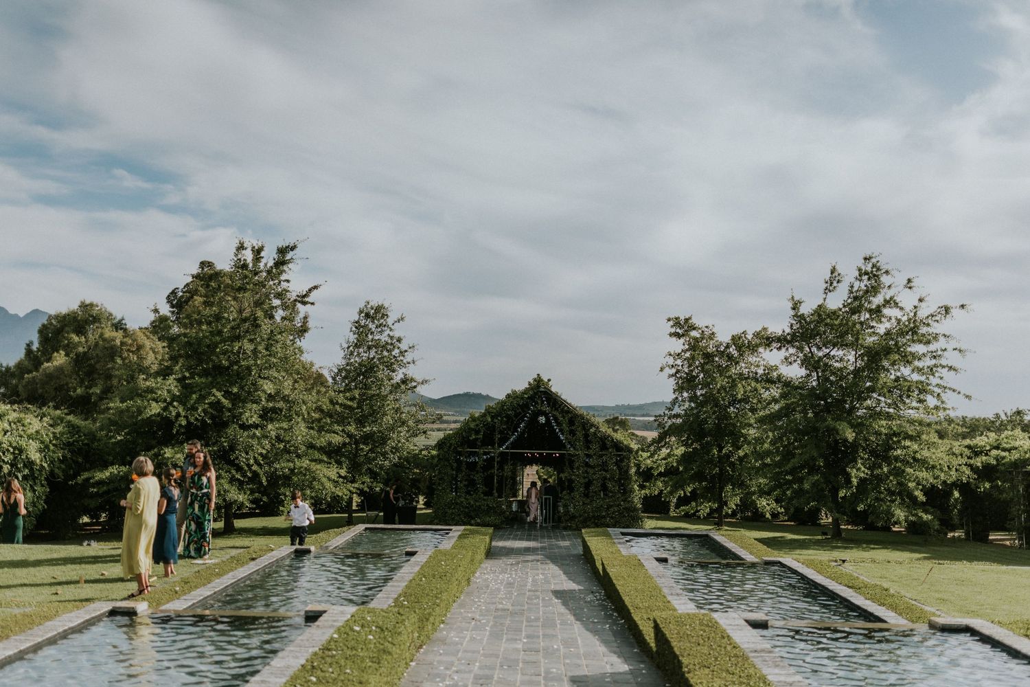 Elegant garden wedding venue with symmetrical reflecting pools, lush greenery, and mountain backdrop.