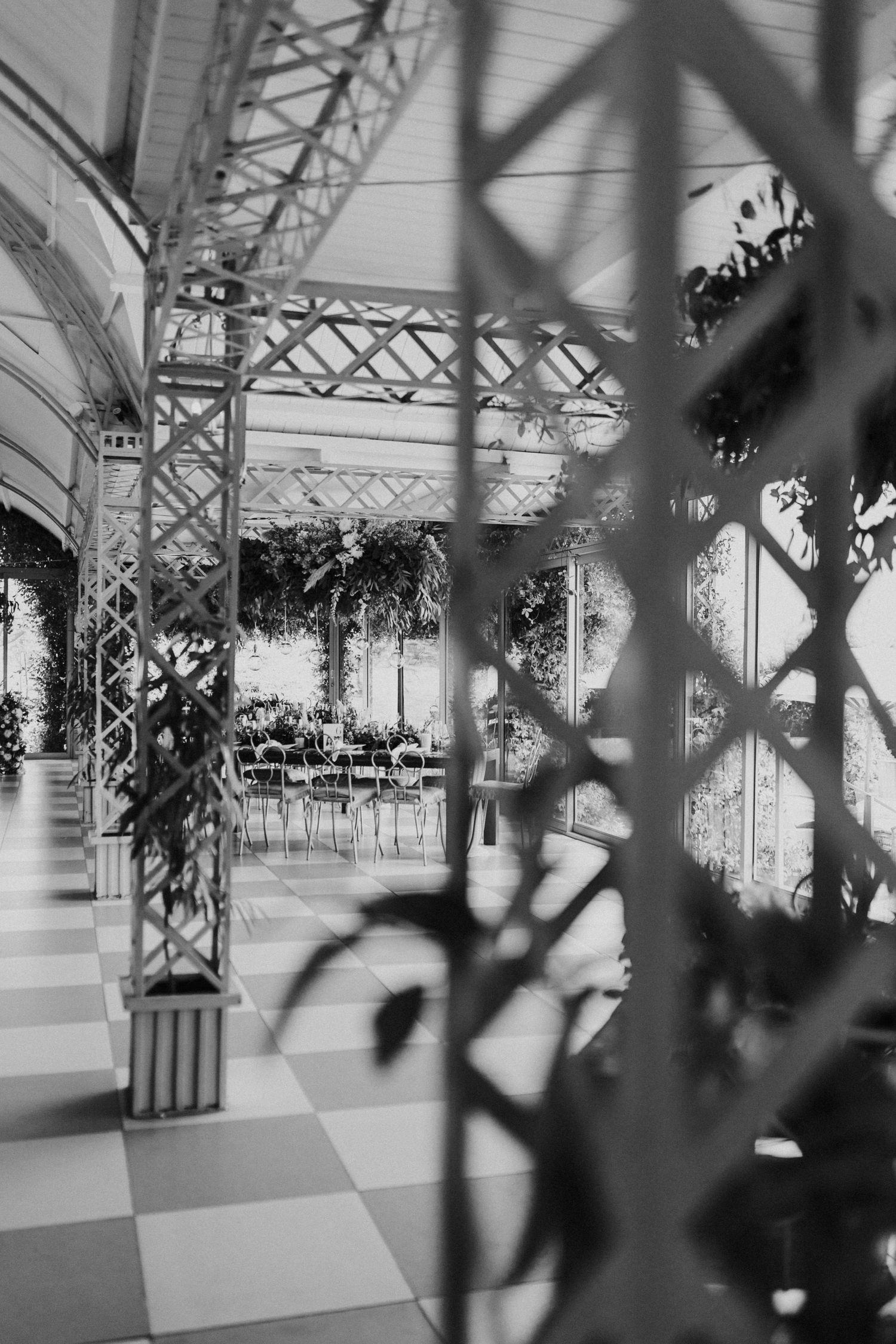 Black and white photo of elegant greenhouse wedding venue with white lattice structures, checkered floors, and lush greenery.