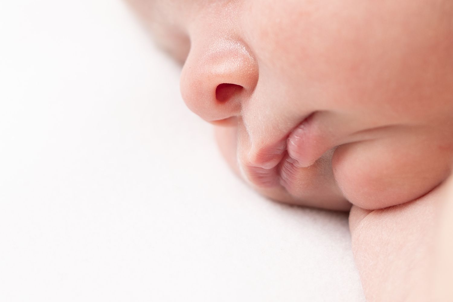 Close-up details of a side-sleeping newborn's pink cheeks, nose, and lips captured in soft natural light.