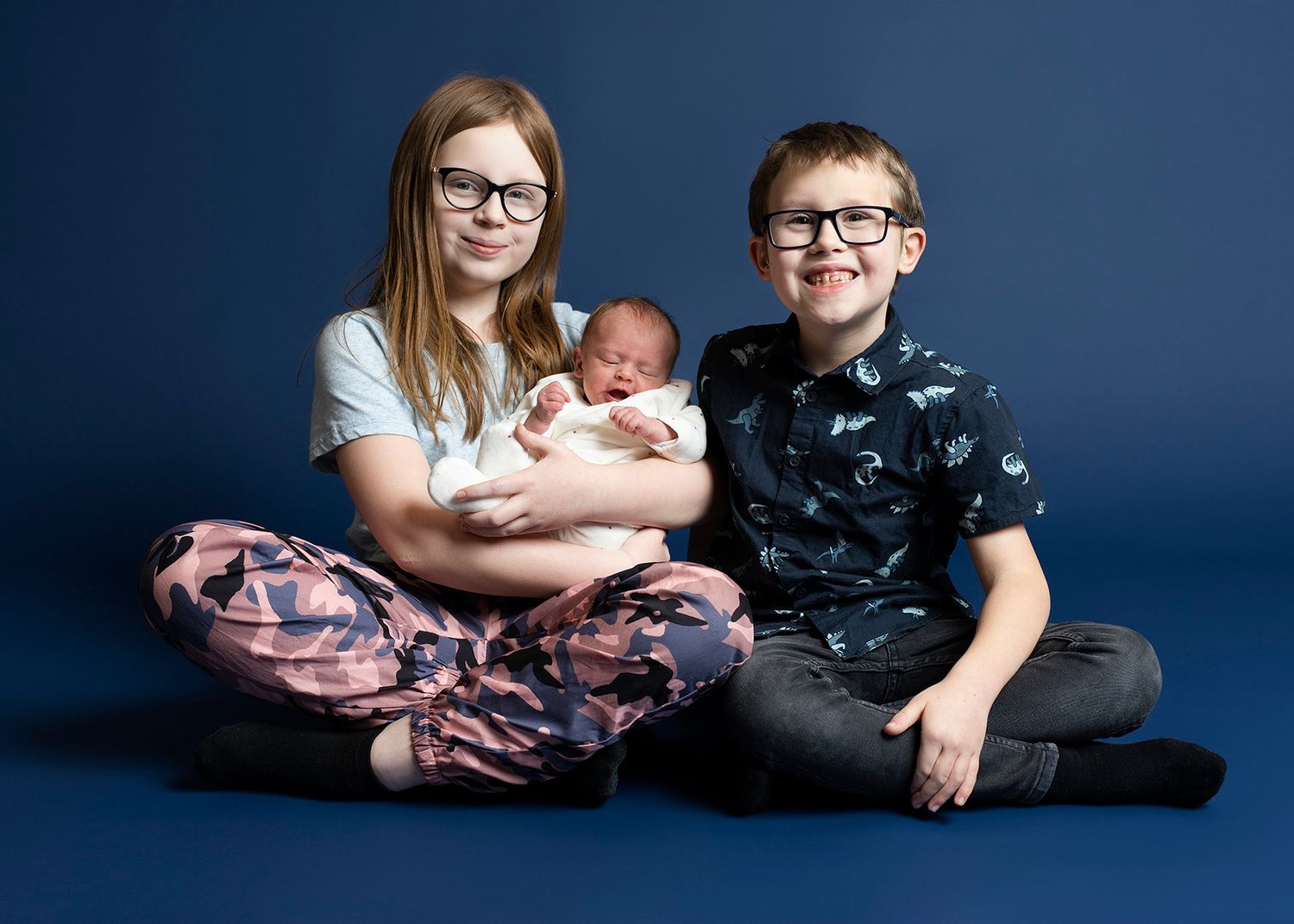 Three people sitting together against a dark blue background in a studio portrait setting.
