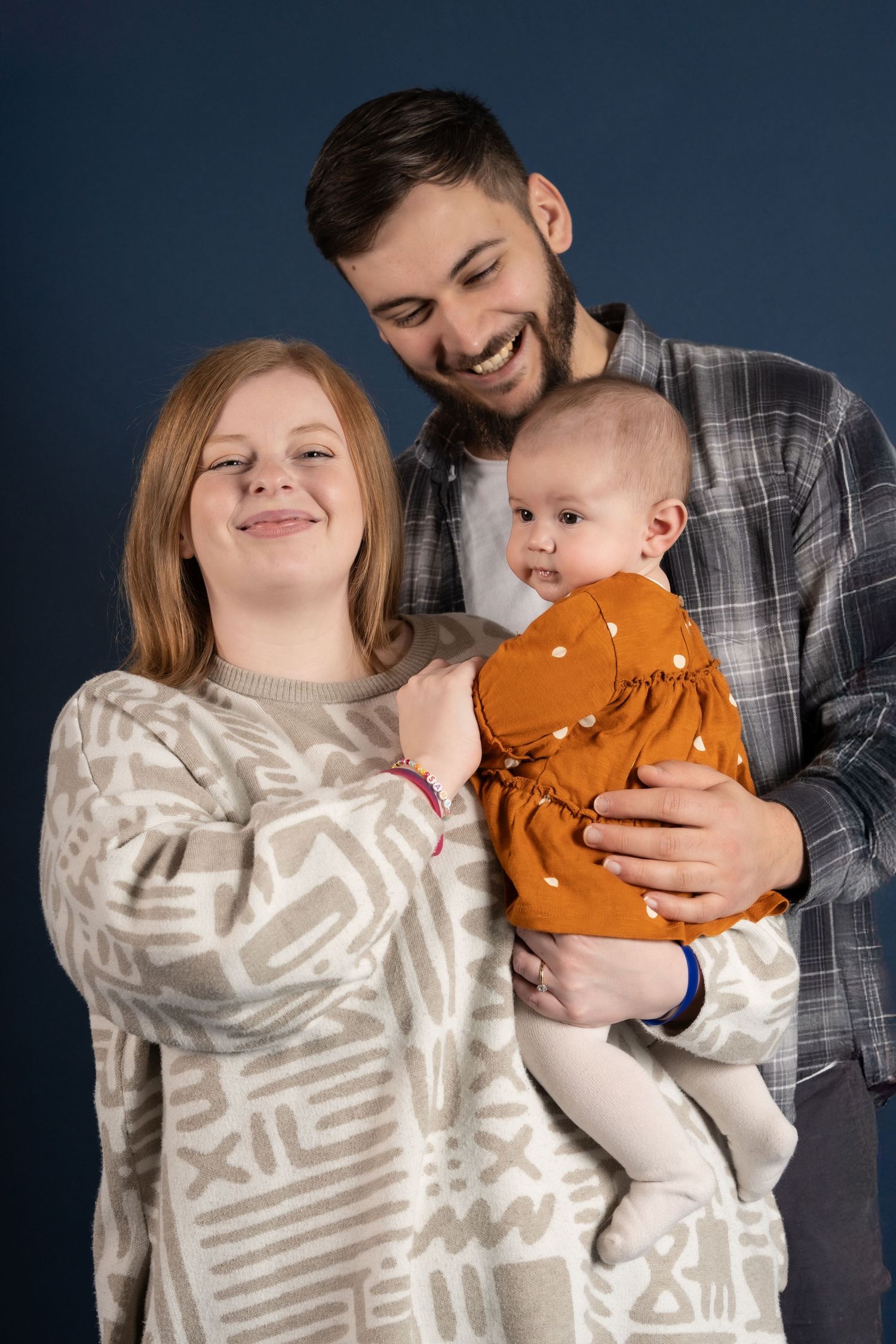 Parent and baby share playful moments in matching outfits for a studio photoshoot series against a dark blue backdrop.