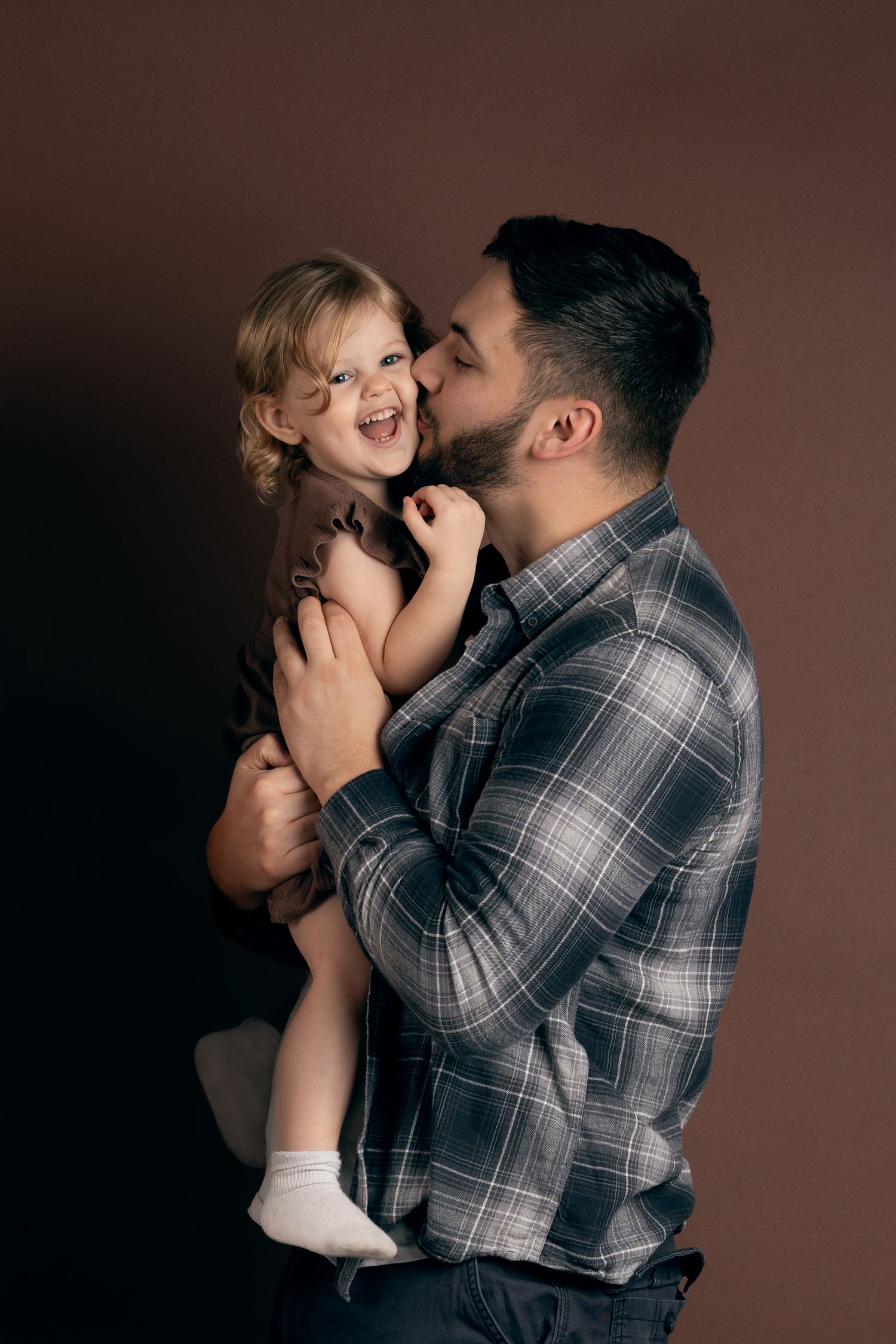 A tender moment between a parent in a plaid shirt and young child against a dark background.