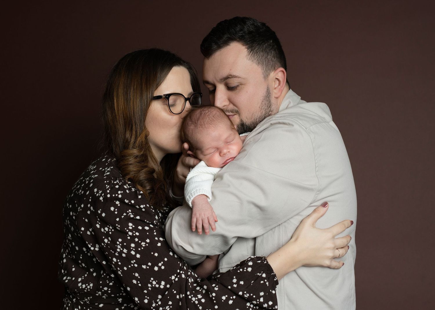 A couple embraces tenderly in a series of intimate portraits against a dark brown backdrop.