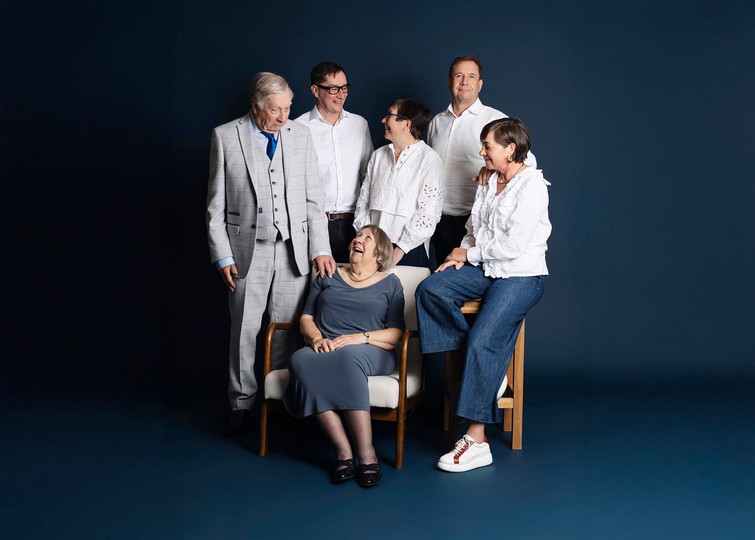A group of people in casual and formal attire sit together against a dark blue studio background.
