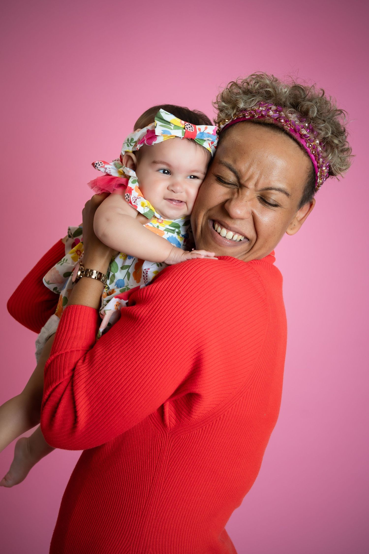 A joyful moment captured against a pink backdrop with matching floral headbands and a bright red sweater.
