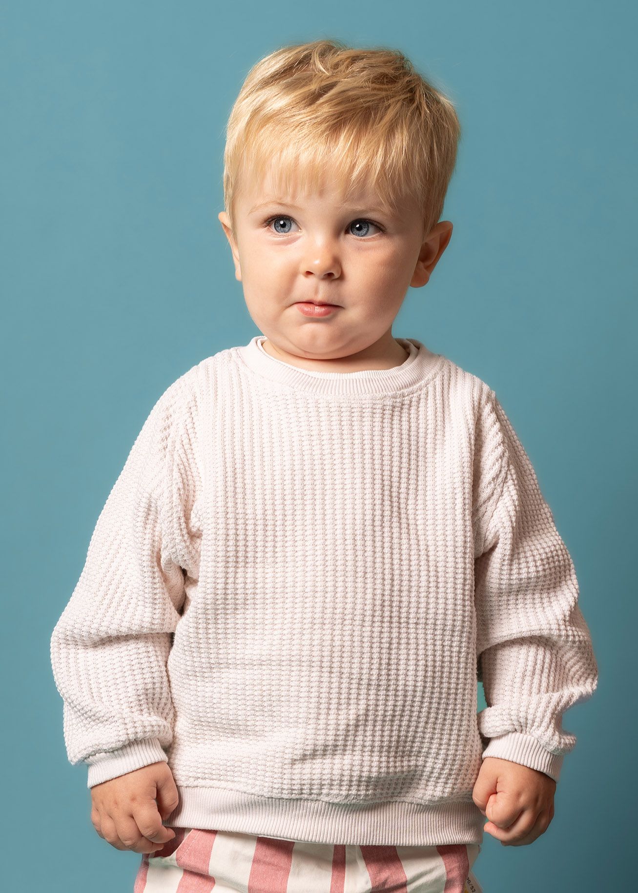 Young child wearing a cozy white waffle knit sweater against a turquoise blue background for a birthday session in Jackfield Telford