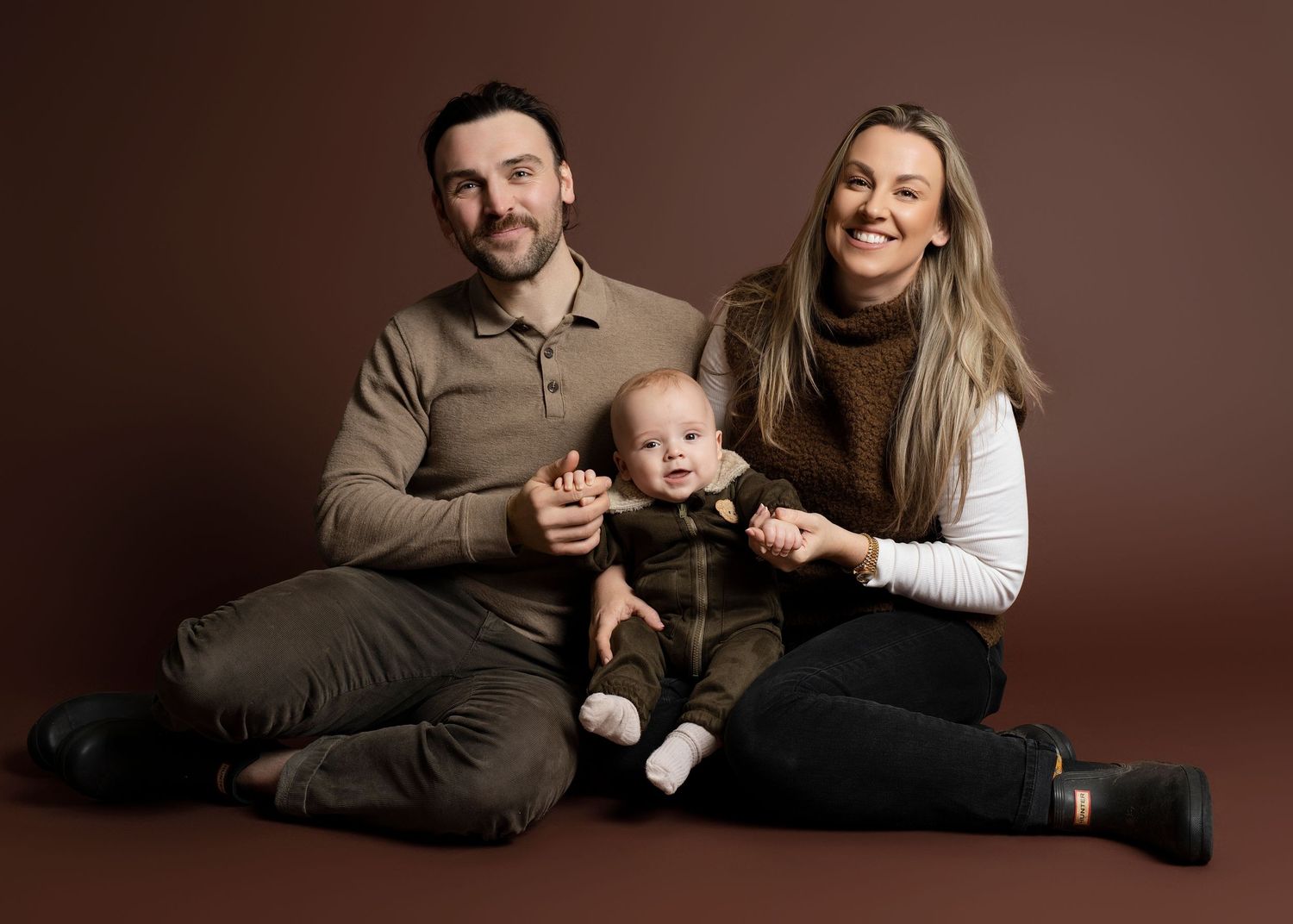 A family poses together on a brown backdrop in a series of candid studio portraits showing warmth and connection.