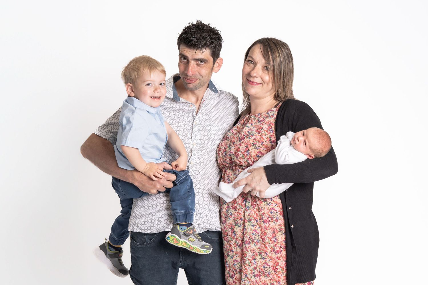 Family of four wearing white and floral outfits pose together in a bright studio setting.