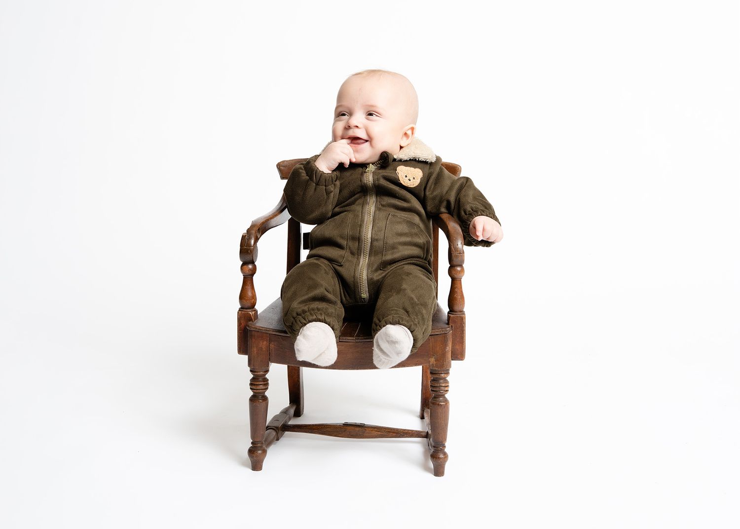 Baby in brown outfit sits on small wooden chair against white background in studio portrait near Shrewsbury