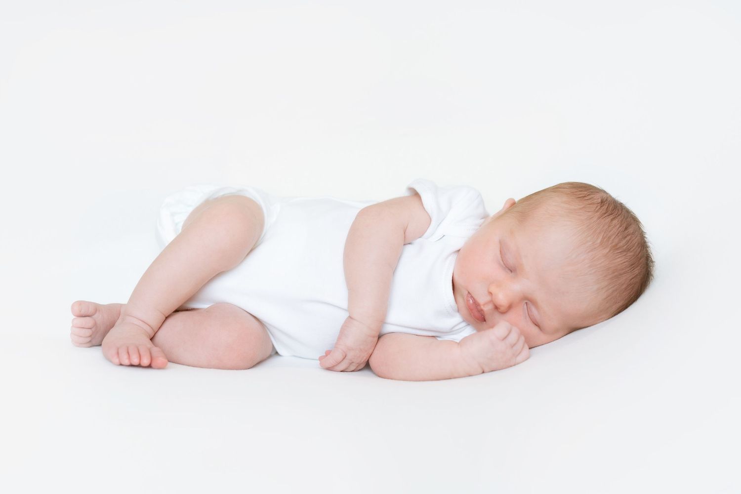 Artistic side view of newborn baby sleeping peacefully on a soft white background in pure white studio setting.