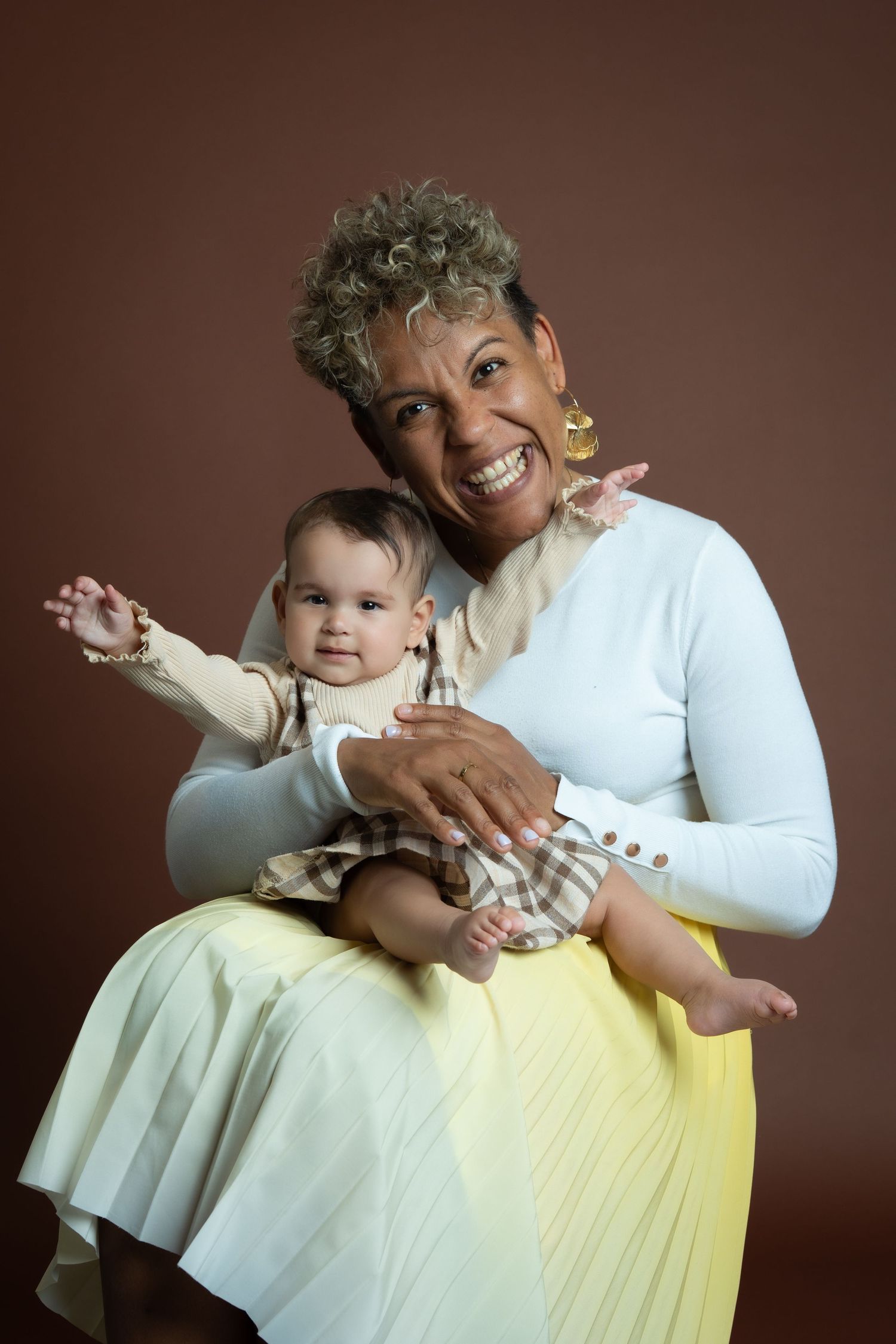 Heartwarming portrait of adult and baby in contrasting white and yellow outfits against a brown studio background.