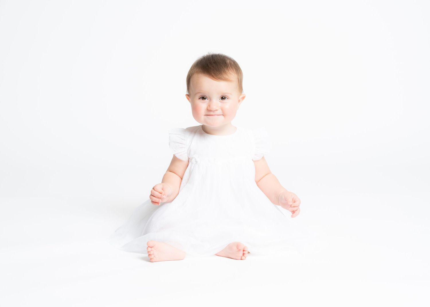 A baby in a white onesie crawls and plays on a bright white background.