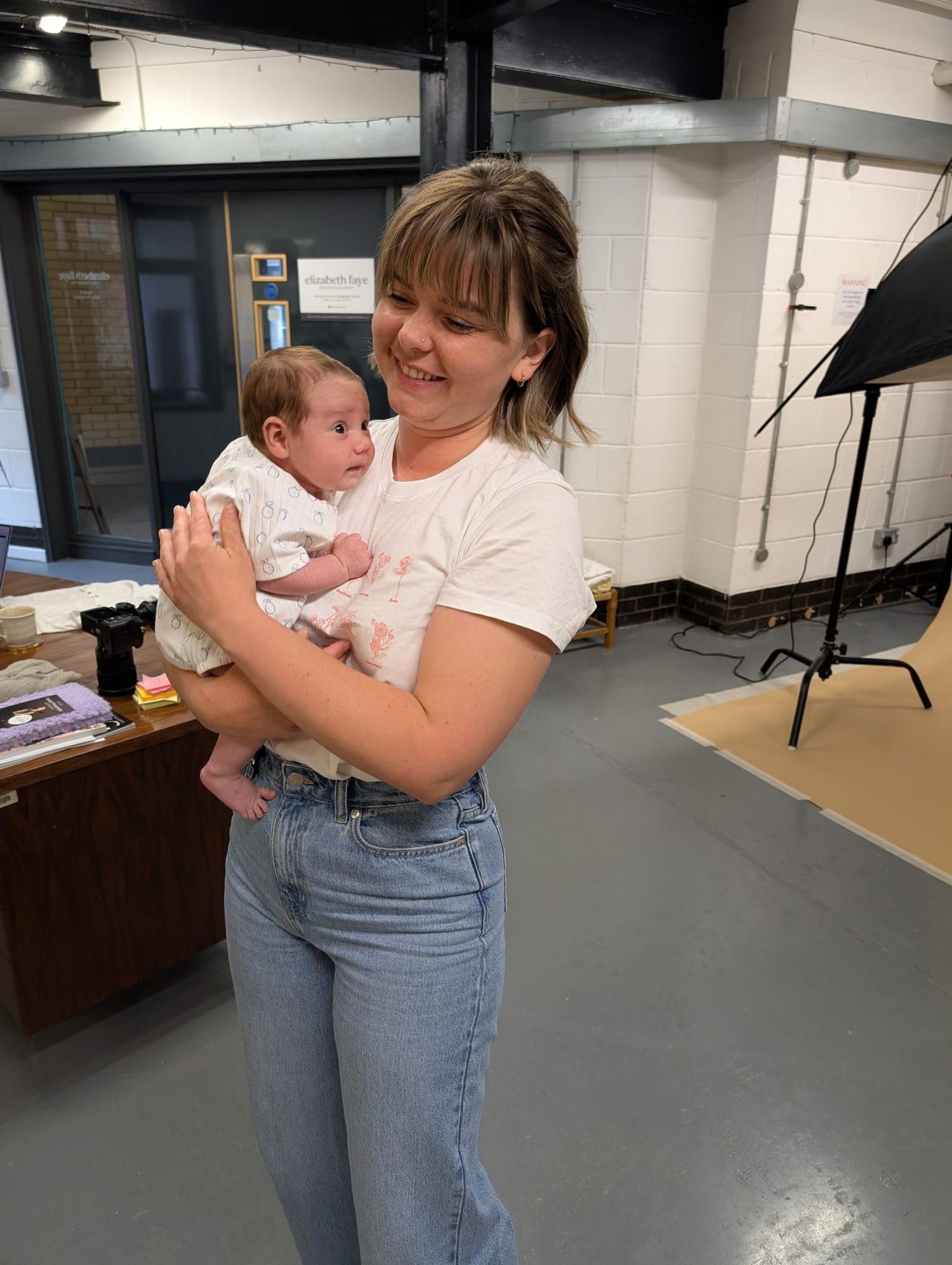 A toddler being held and comforted in an indoor space with studio lighting equipment visible in the background.