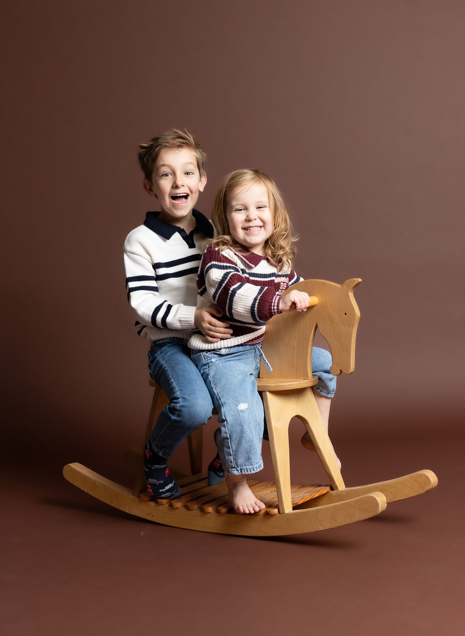 Siblings playing together on a wooden rocking horse against a brown backdrop in Telford