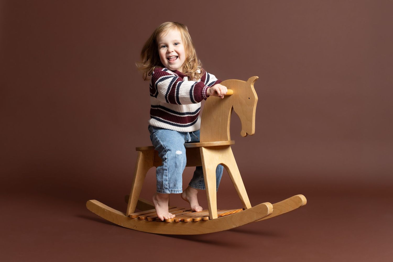 A child plays on a wooden rocking horse toy against a minimalist brown studio backdrop in Telford