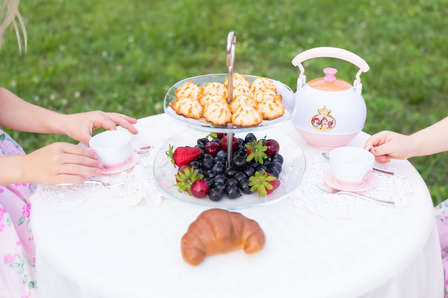 A tea party spread with grapes, croissants and snacks on a white tablecloth outdoors for a mini session photoshoot in Pittsburg Kansas.