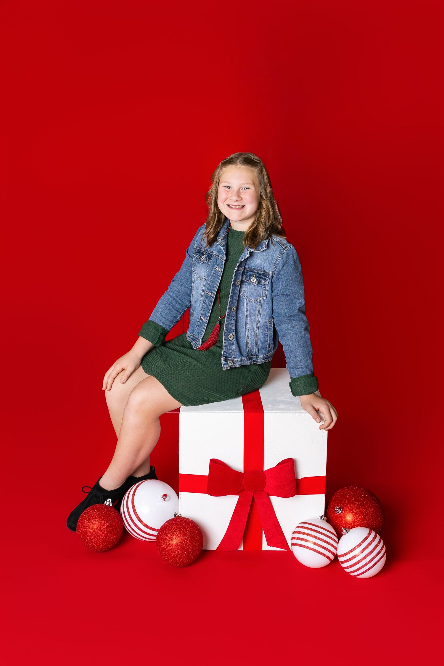 A bright red background featuring candy cane striped ornaments and wrapped presents during Christmas photos in Pittsburg Ks and Joplin MO.