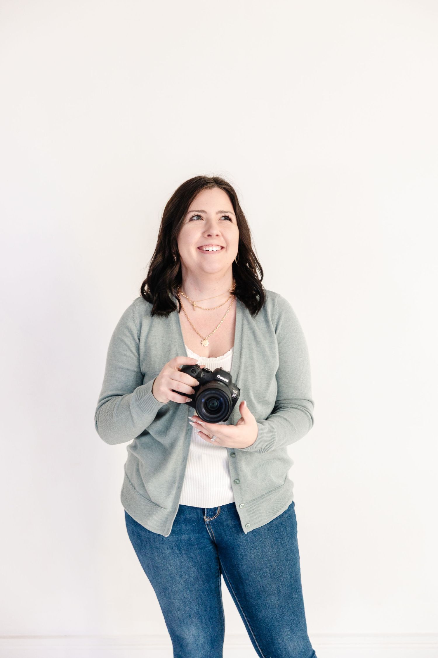 Pittsburg KS and Joplin MO Brand and Family Photographer in blue jeans and green cardigan poses with camera during a branding photoshoot.