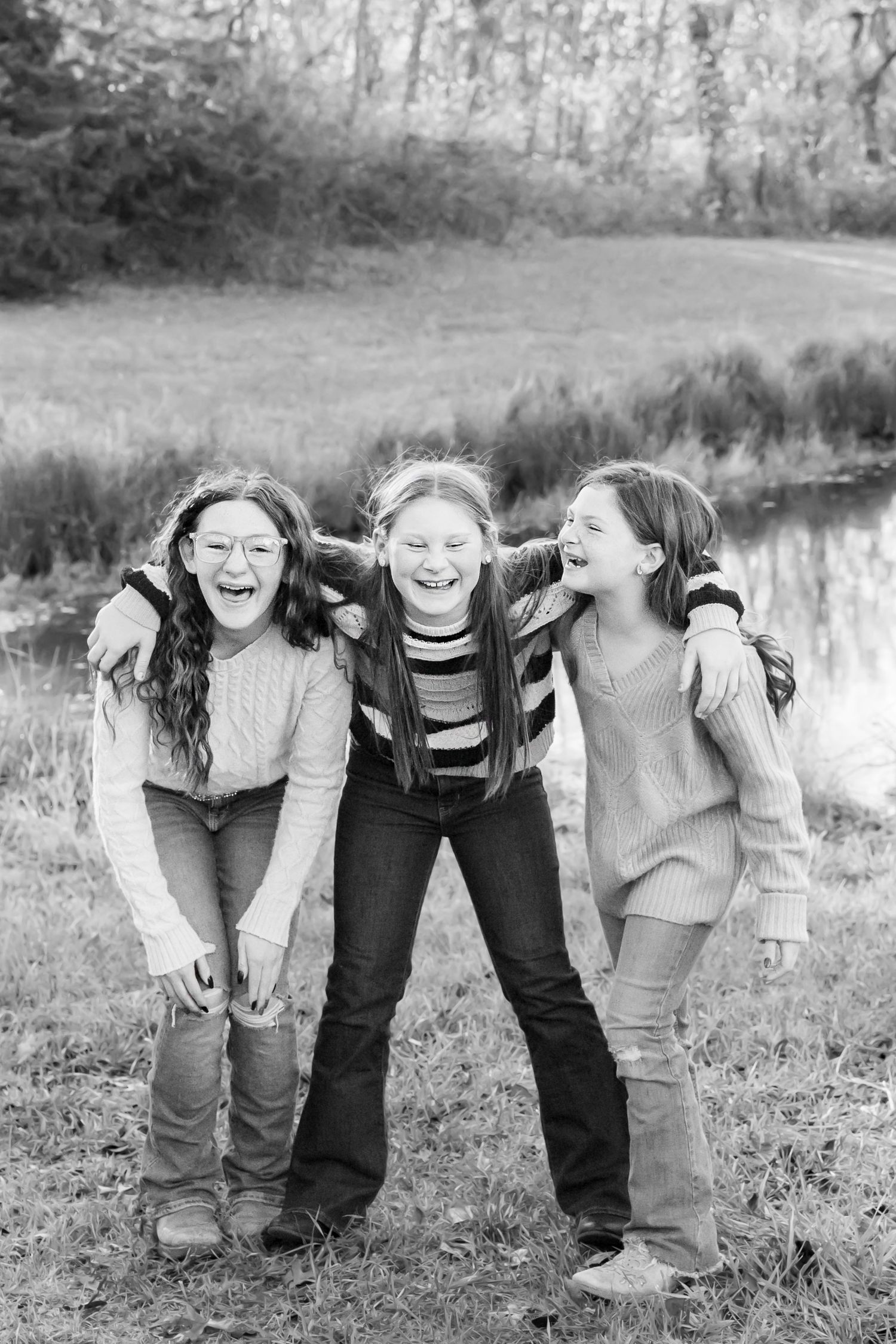 Three children embrace and laugh together outdoors in a joyful black and white candid moment.