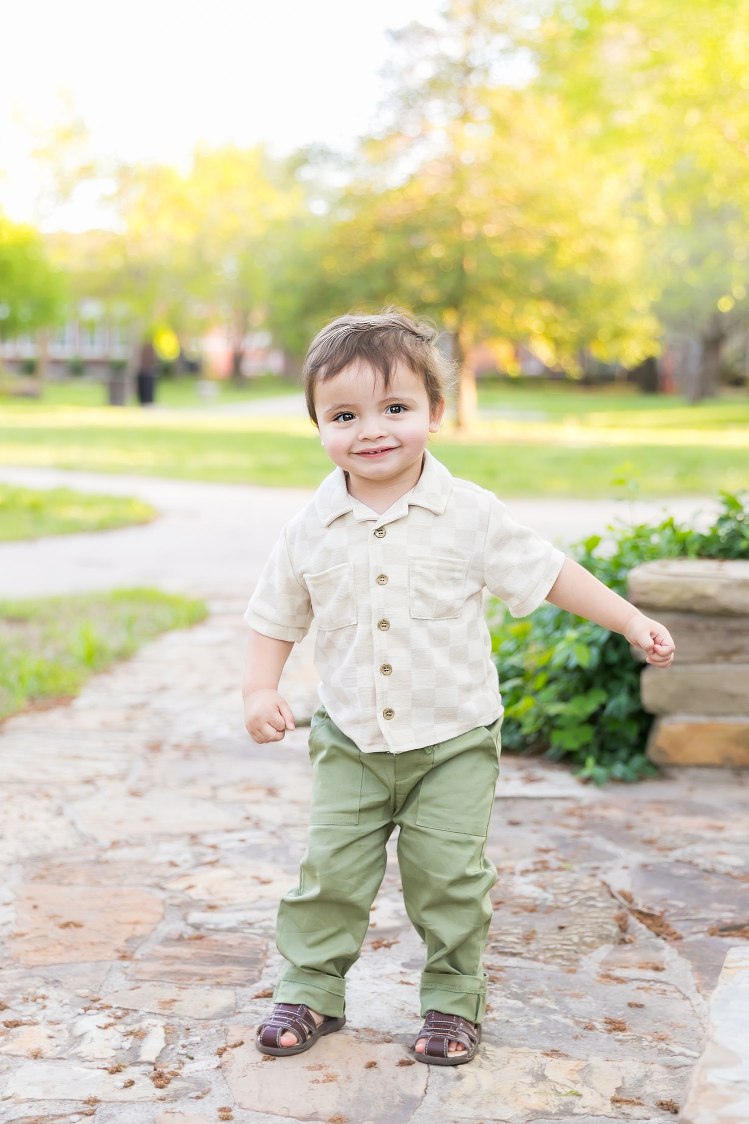 Small child stands on a stone path smiling during an outdoor birthday photoshoot at Pitt State University in Pittsburg Ks.