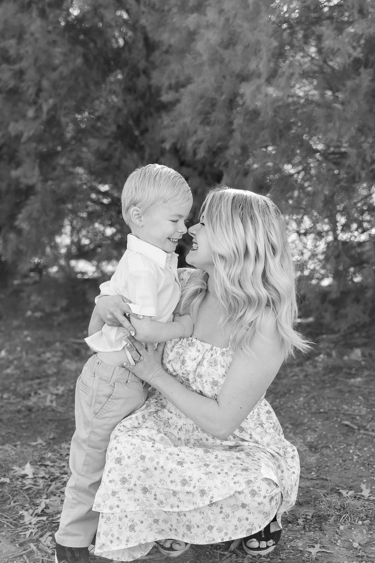 A tender black and white portrait of a parent and child sharing an intimate moment outdoors in a floral dress.