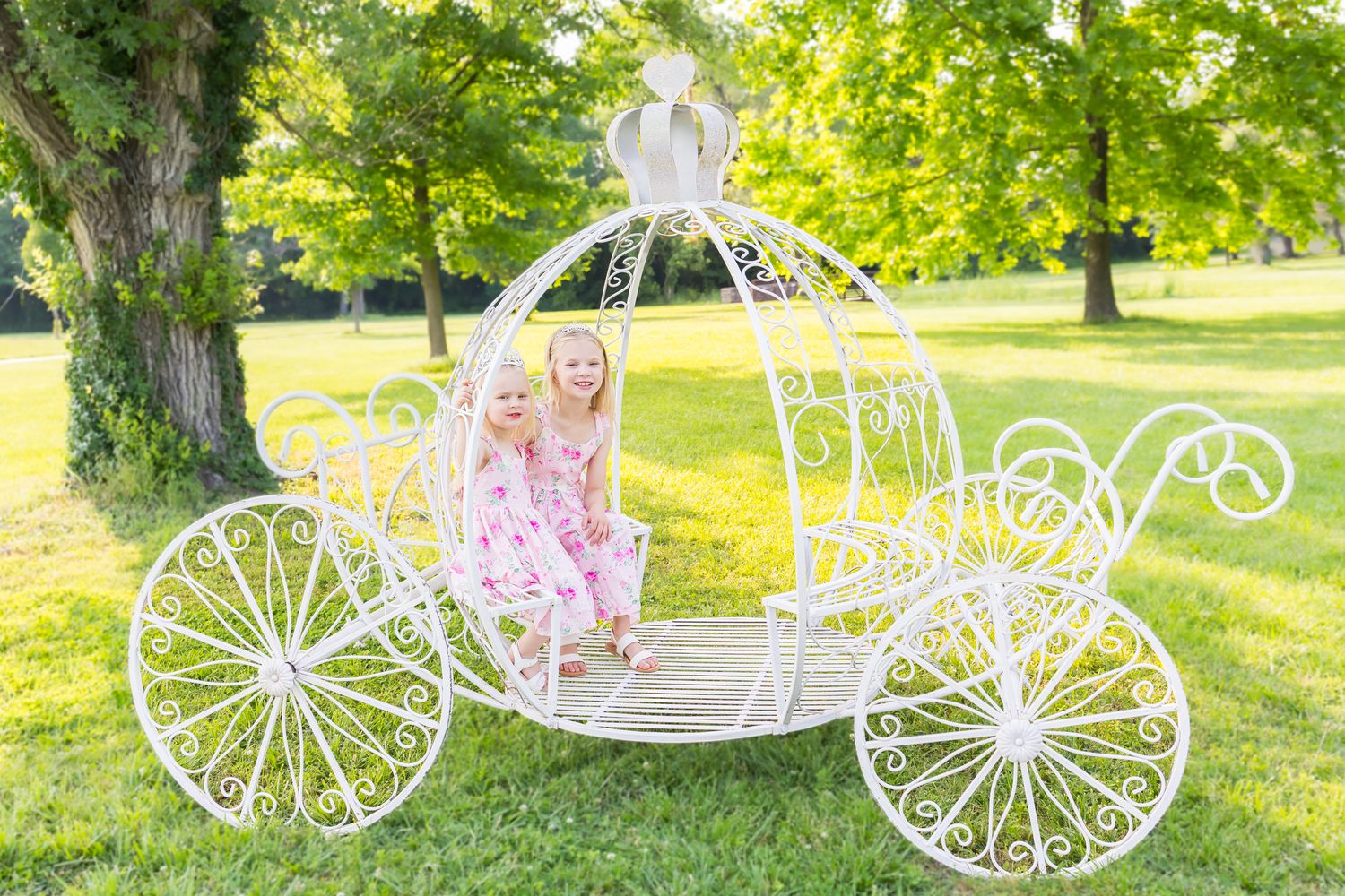 Two sisters sit inside a large white carriage posing during a princess mini session photoshoot in Pittsburg Kansas.