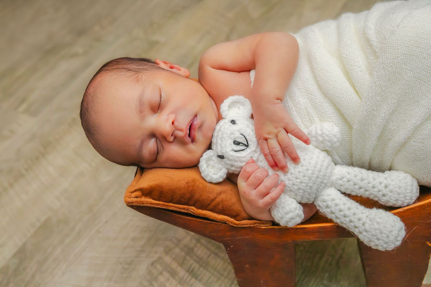 Peaceful sleeping newborn cuddles with white knitted teddy bear while resting in wooden bowl.