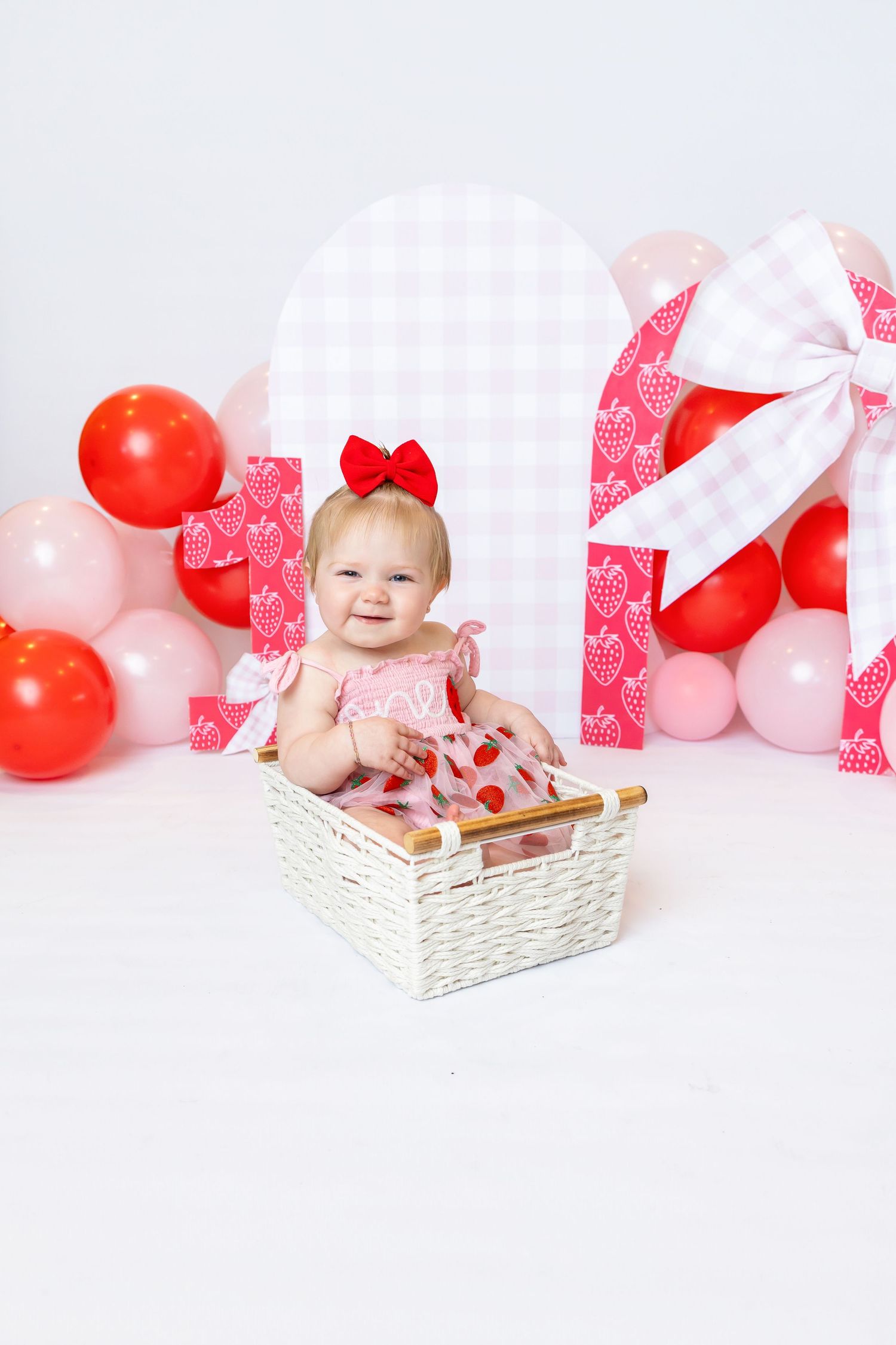 Baby sits in basket wearing a strawberry pink dress during 1st birthday shoot with Annie Robinson Photography of Pittsburg KS and Joplin Mo.