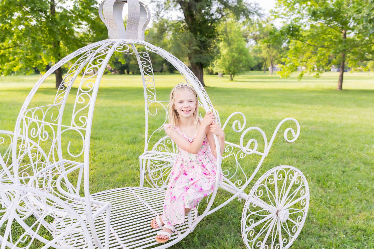 A young child wearing pink dress poses sitting inside large white carriage during a princess mini session photoshoot in Pittsburg Kansas.