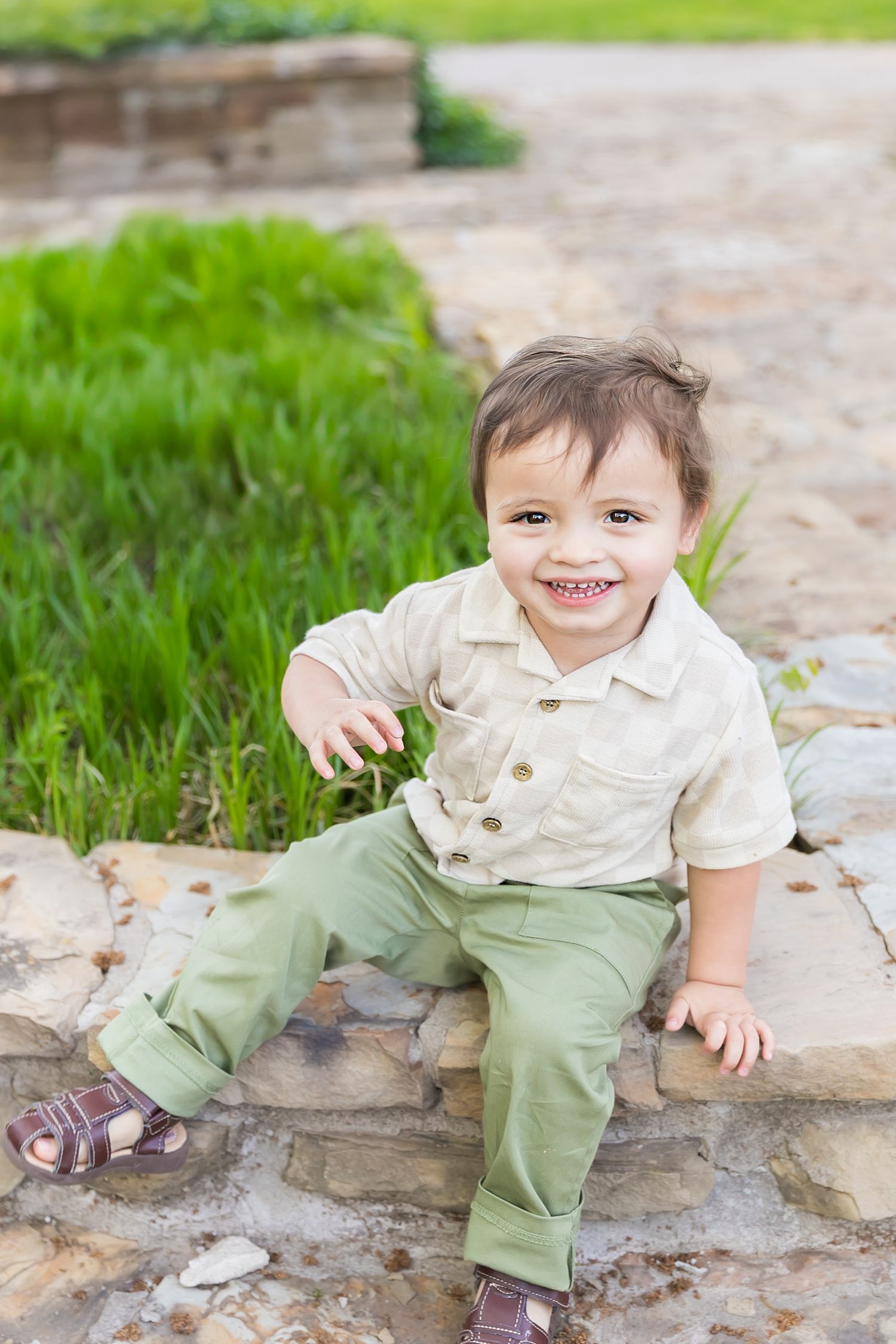 A small child sits on a stone wall smiling for 2 year old milestone birthday photos at Pitt State University in Pittsburg KS.