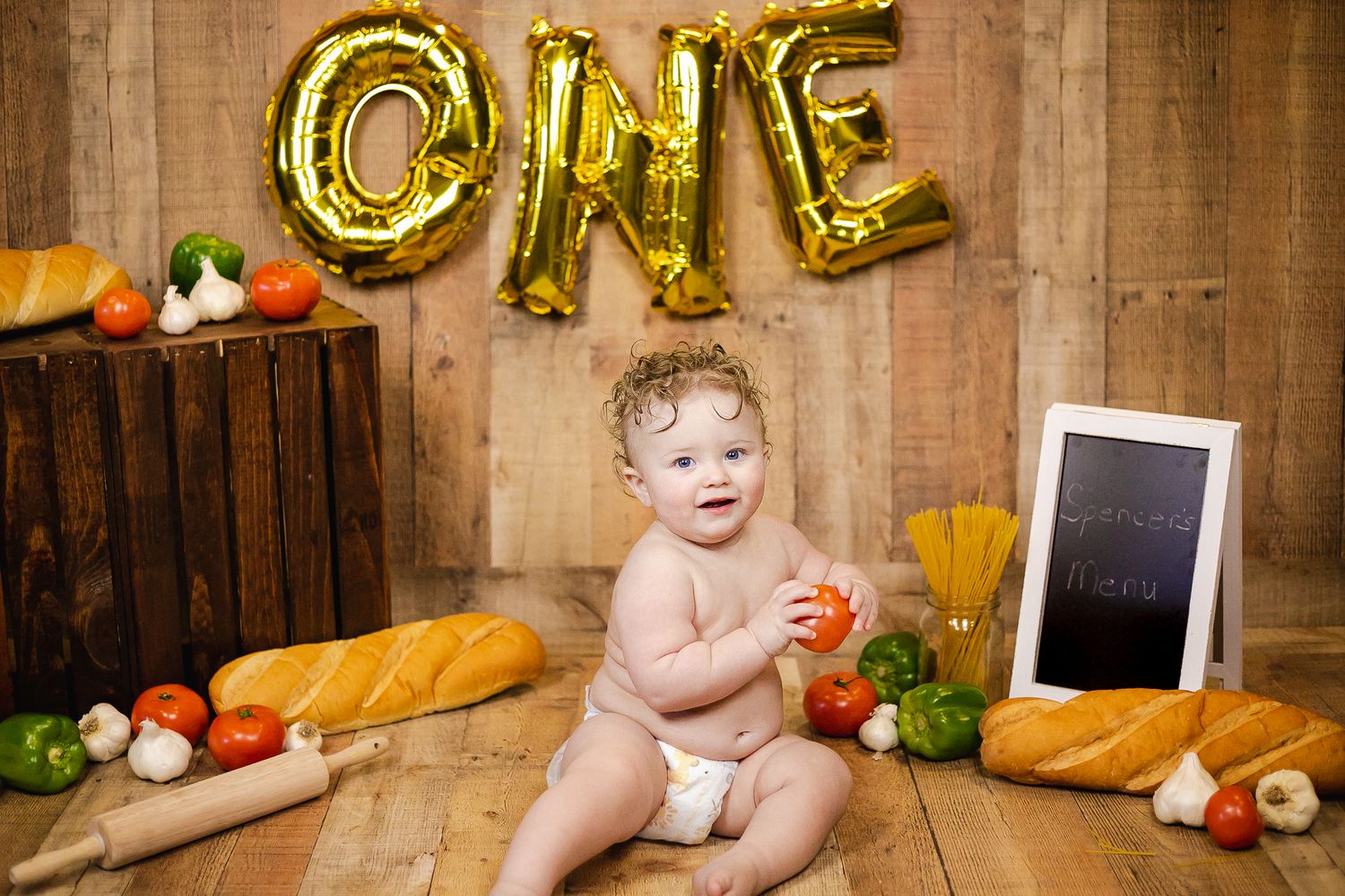 Fall themed first birthday photo setup with balloon letters, vegetables and wooden backdrop.